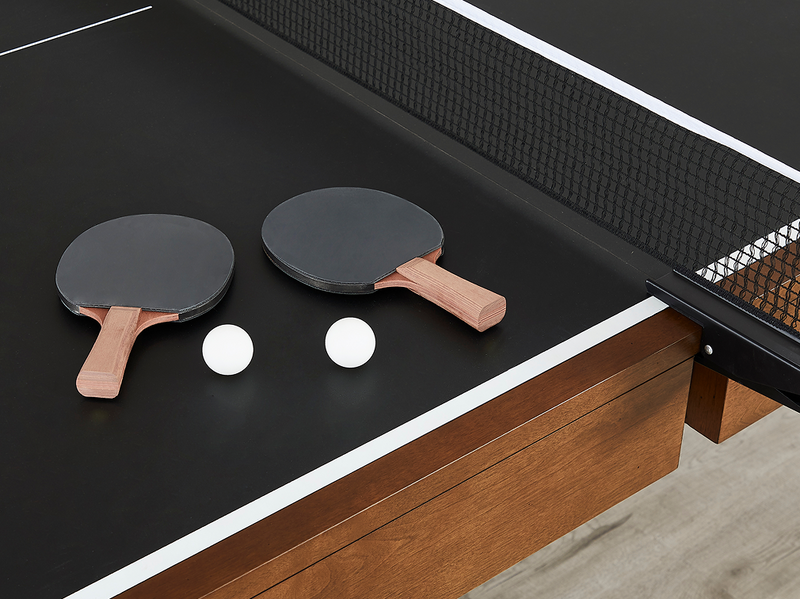 A black table tennis table with two wooden paddle-rackets and two white ping-pong balls on a black court surface, shown in a clean interior setting.