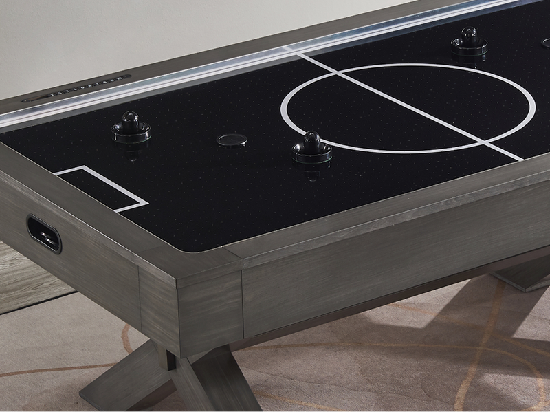 A close-up of an air hockey table showing a black playing surface with white field markings and a gray wood-grain frame and legs.